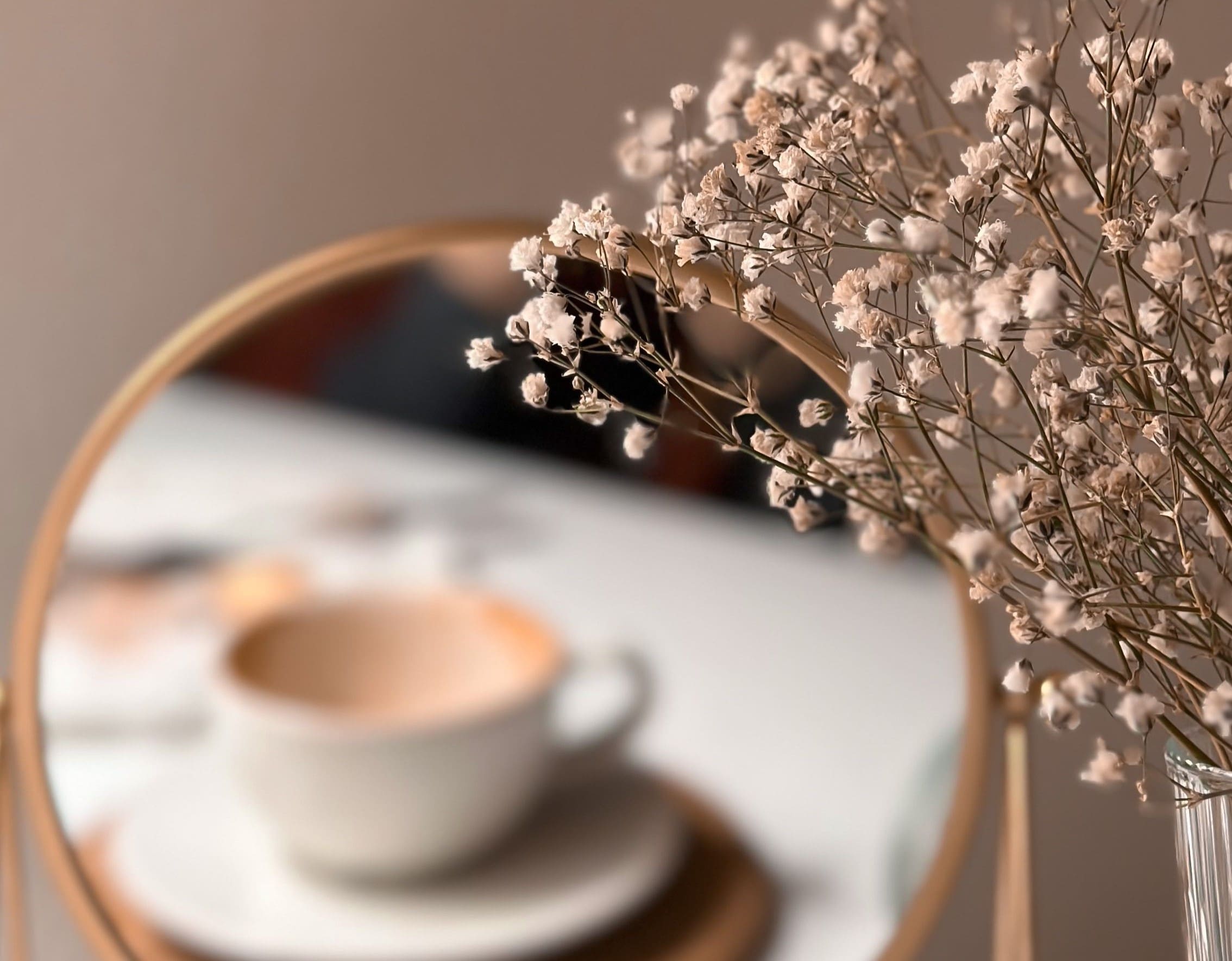 Minimal beige aesthetic still life with baby’s breath flowers beside a mirror reflecting a coffee cup, representing women’s hormone health, PCOS, and metabolic balance awareness.